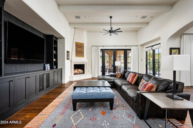 living room featuring a large fireplace, ceiling fan, beamed ceiling, and dark wood-type flooring