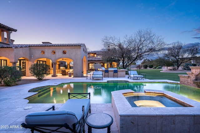 pool at dusk with an in ground hot tub, a patio area, and a yard