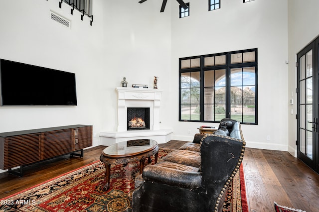 living room with ceiling fan, a towering ceiling, and dark hardwood / wood-style floors