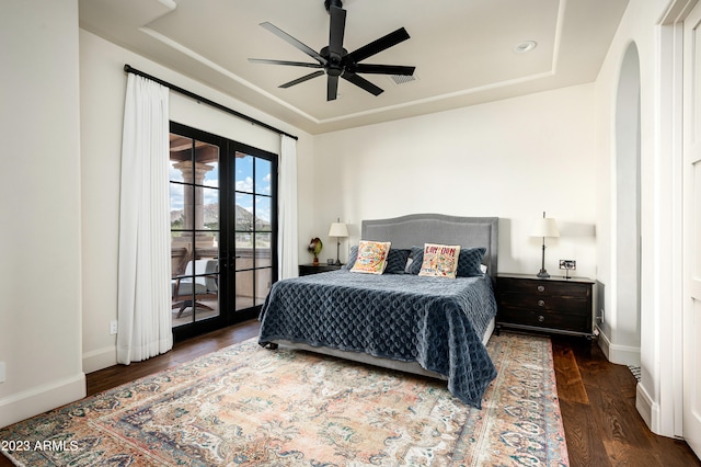 bedroom with a tray ceiling, dark hardwood / wood-style flooring, ceiling fan, and french doors