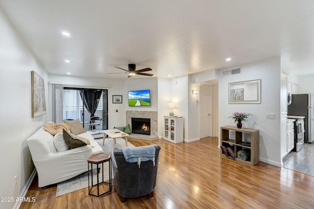 living area featuring light wood-style floors, a warm lit fireplace, baseboards, and recessed lighting