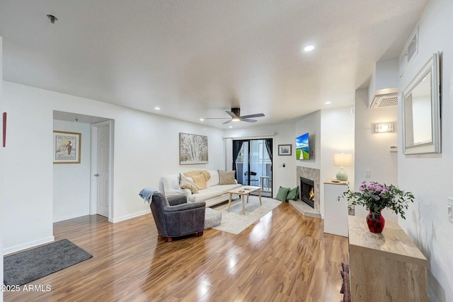 living area with a warm lit fireplace, light wood-type flooring, visible vents, and recessed lighting