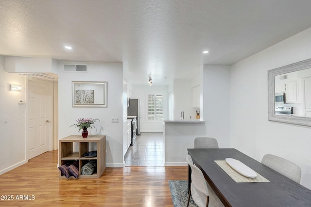 dining room featuring light wood finished floors, baseboards, visible vents, a textured ceiling, and recessed lighting