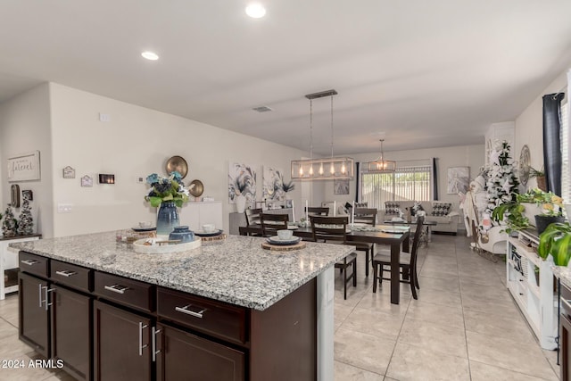 kitchen featuring pendant lighting, a center island, light stone countertops, light tile patterned floors, and dark brown cabinetry