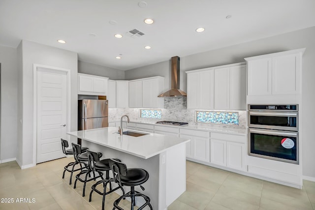 kitchen with stainless steel appliances, visible vents, decorative backsplash, a sink, and wall chimney exhaust hood