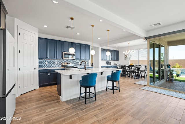 kitchen with hanging light fixtures, appliances with stainless steel finishes, beam ceiling, a center island with sink, and a breakfast bar area