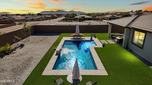 pool at dusk featuring pool water feature, a patio area, and a lawn