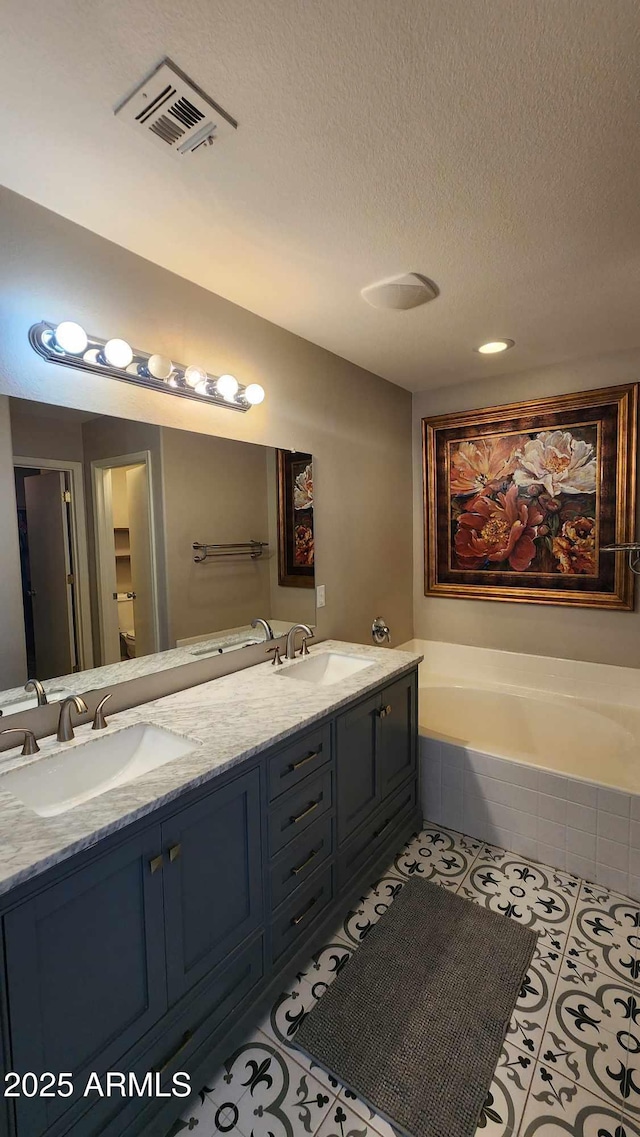 bathroom with tile patterned flooring, vanity, a textured ceiling, and tiled tub