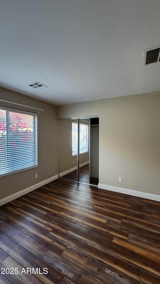 unfurnished bedroom with dark hardwood / wood-style flooring, a textured ceiling, and a closet