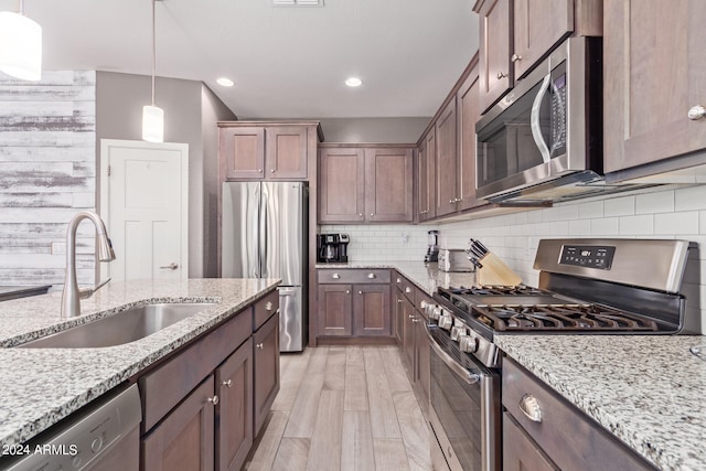 kitchen with light wood-type flooring, sink, tasteful backsplash, appliances with stainless steel finishes, and light stone countertops