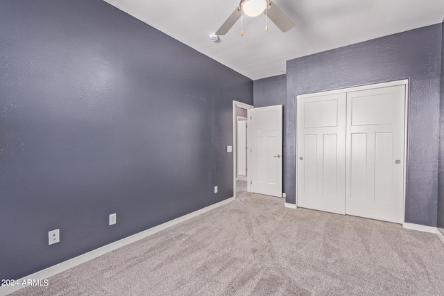 unfurnished bedroom with ceiling fan, vaulted ceiling, a closet, and carpet flooring