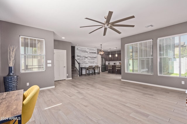 living room with ceiling fan with notable chandelier, light hardwood / wood-style floors, and a wealth of natural light