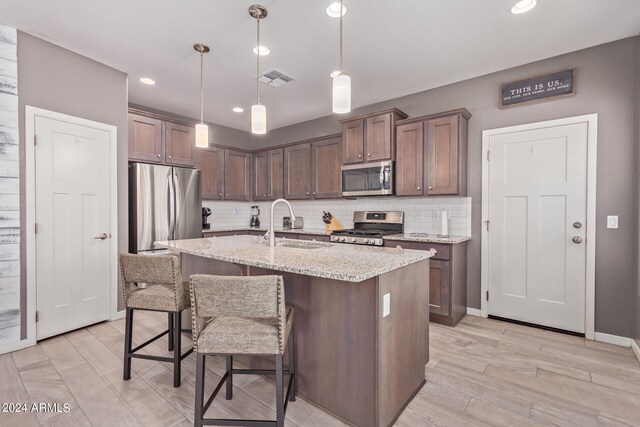 kitchen with sink, decorative light fixtures, stainless steel appliances, light stone countertops, and decorative backsplash