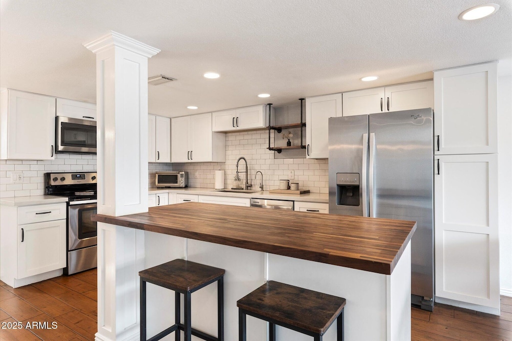 kitchen with a center island, sink, butcher block countertops, white cabinetry, and stainless steel appliances