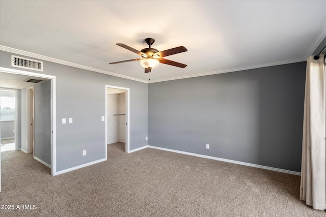 unfurnished bedroom featuring ceiling fan, crown molding, a spacious closet, and carpet floors