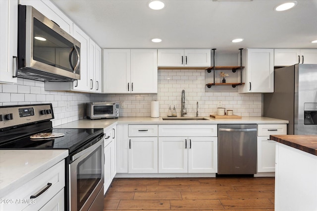 kitchen with hardwood / wood-style floors, white cabinets, sink, decorative backsplash, and stainless steel appliances