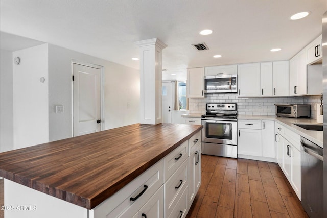 kitchen featuring white cabinets, a center island, butcher block counters, and stainless steel appliances