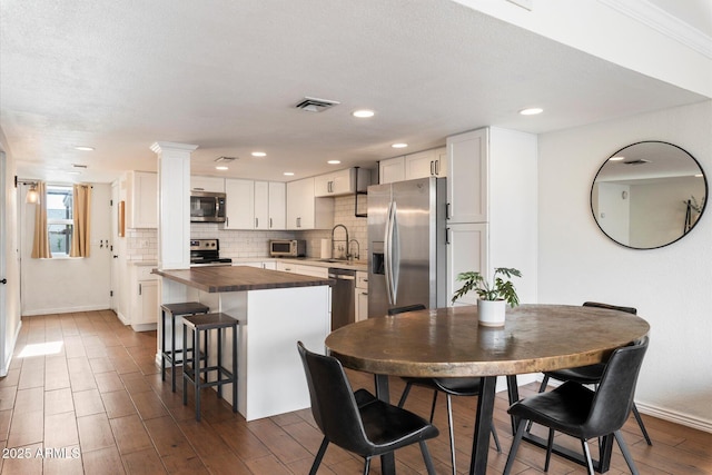 kitchen with a kitchen bar, stainless steel appliances, a kitchen island, butcher block countertops, and white cabinetry