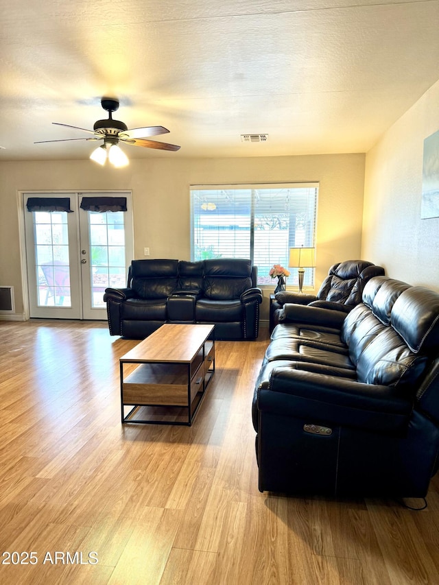 living room with a textured ceiling, ceiling fan, visible vents, french doors, and light wood finished floors