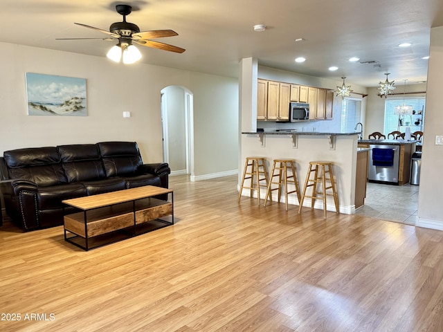 living room with arched walkways, baseboards, light wood-style flooring, ceiling fan with notable chandelier, and recessed lighting