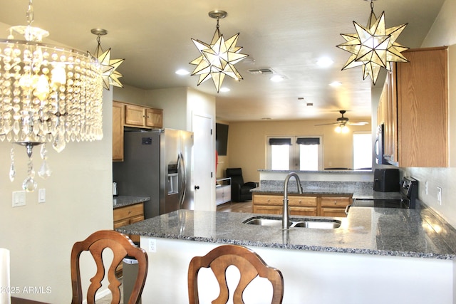 kitchen with decorative light fixtures, stainless steel appliances, a sink, dark stone counters, and a peninsula