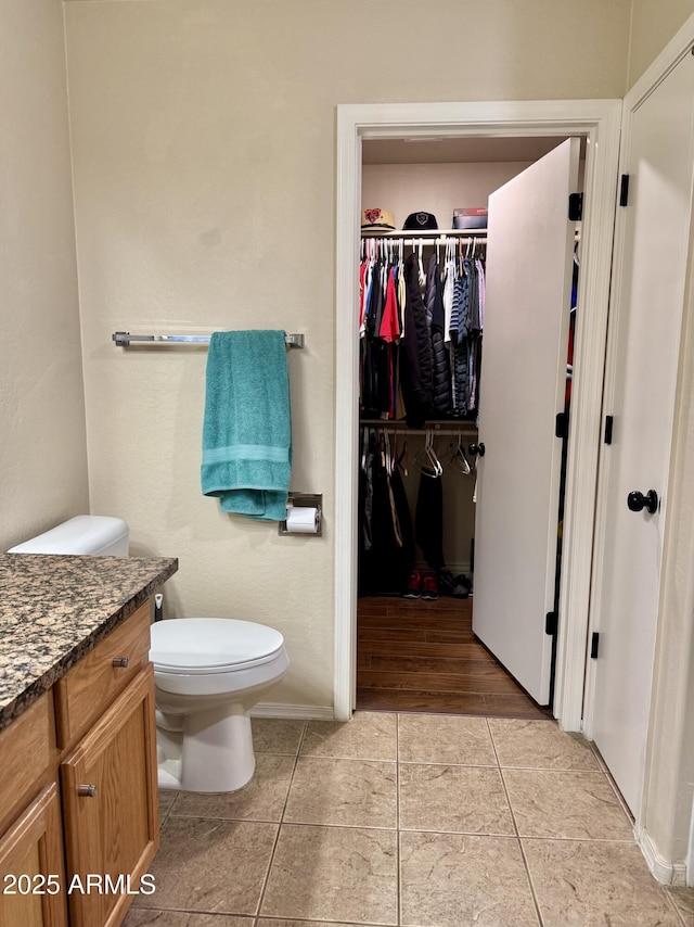 bathroom featuring toilet, tile patterned floors, a spacious closet, and vanity