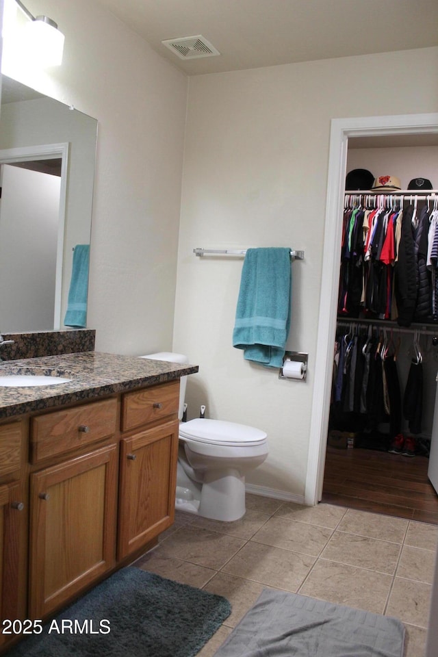 bathroom featuring toilet, vanity, visible vents, tile patterned floors, and a walk in closet