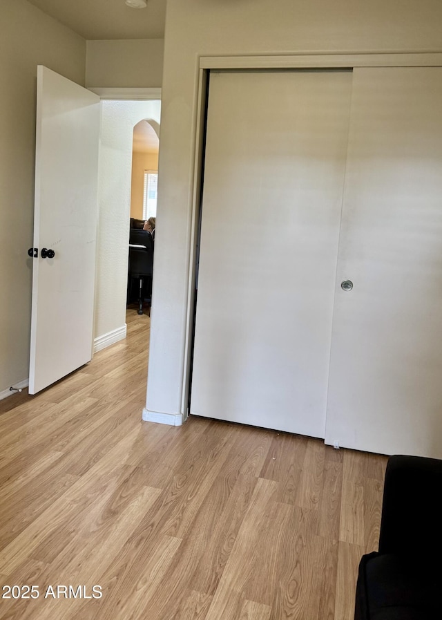 unfurnished bedroom featuring light wood finished floors, baseboards, arched walkways, and a closet