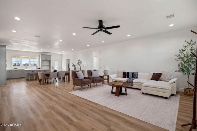 living area with light wood-style floors, ceiling fan, visible vents, and recessed lighting