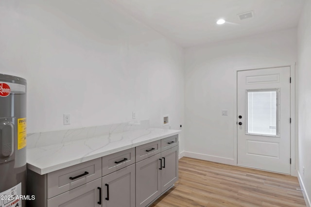 kitchen with light stone counters, baseboards, water heater, light wood-style floors, and gray cabinets