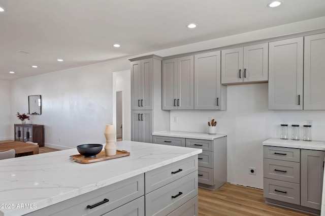 kitchen with light wood-type flooring, recessed lighting, gray cabinetry, and light stone countertops