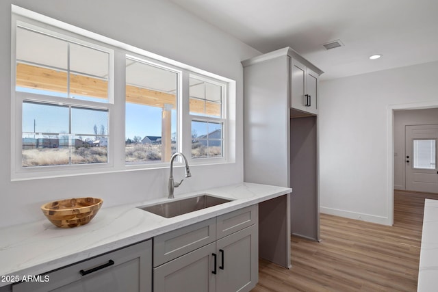 kitchen with visible vents, light wood-style flooring, light stone counters, gray cabinets, and a sink