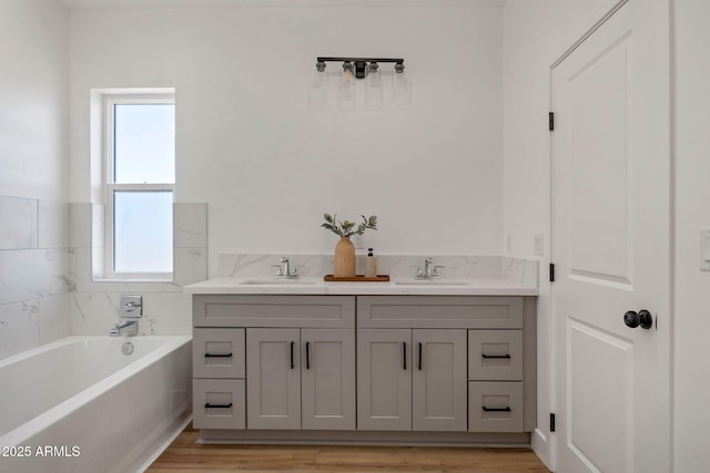 full bath featuring a garden tub, double vanity, wood finished floors, and a sink