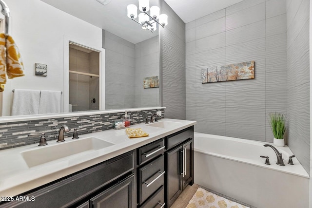 bathroom with shower with separate bathtub, vanity, a chandelier, and tasteful backsplash