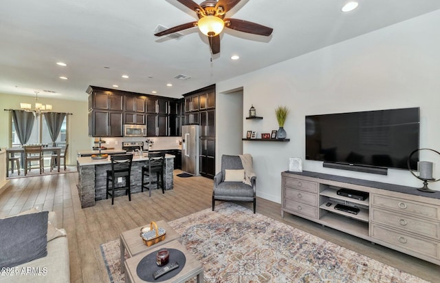 living room featuring light wood-type flooring and ceiling fan with notable chandelier