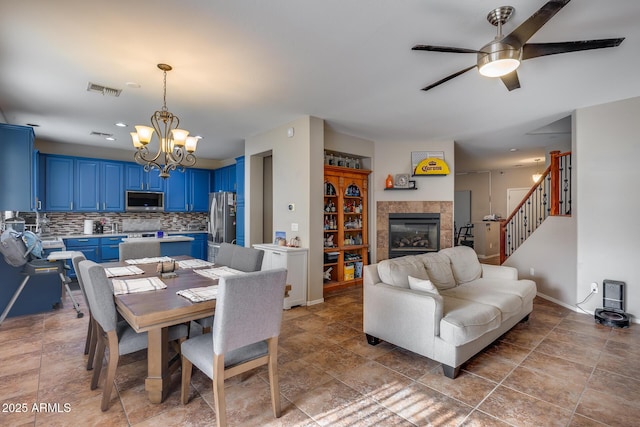 dining area with ceiling fan with notable chandelier and a tile fireplace