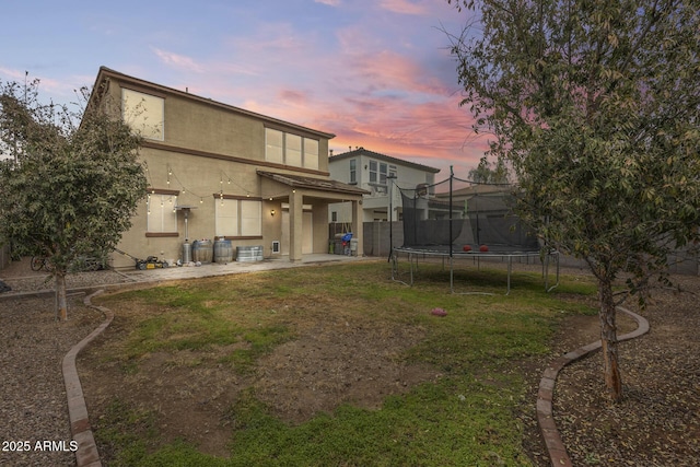 back house at dusk with a lawn, a patio area, and a trampoline