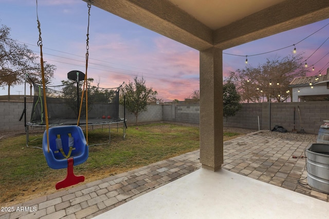 patio terrace at dusk featuring a yard and a trampoline