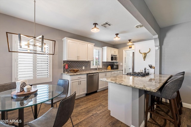 69 W Virginia Ave, Phoenix, AZ 85003 - kitchen with appliances with stainless steel finishes, a chandelier, backsplash, a kitchen bar, and white cabinetry