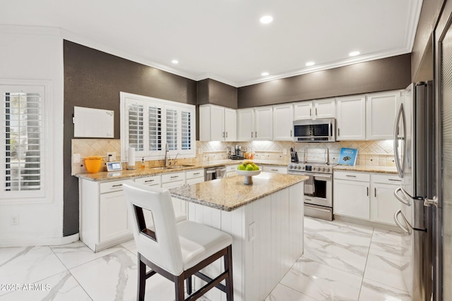 kitchen with stainless steel appliances, white cabinetry, a kitchen island, and light stone counters