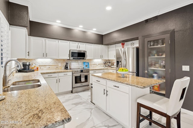 kitchen with sink, appliances with stainless steel finishes, light stone counters, ornamental molding, and white cabinets