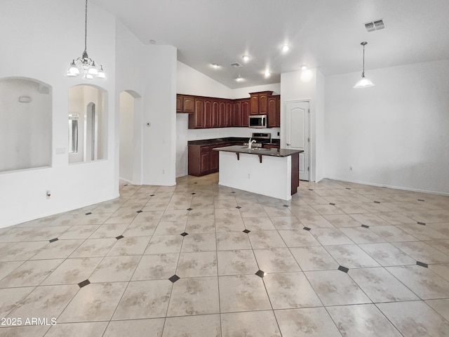 kitchen featuring appliances with stainless steel finishes, an inviting chandelier, high vaulted ceiling, light tile patterned floors, and a center island with sink