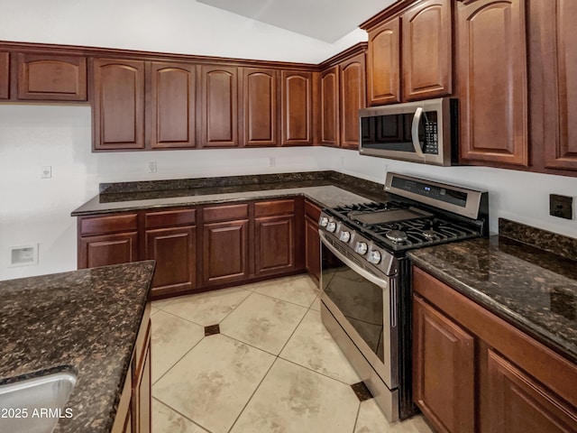 kitchen with light tile patterned floors, appliances with stainless steel finishes, lofted ceiling, and dark stone counters