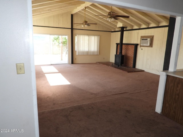 unfurnished living room featuring carpet floors, a wood stove, vaulted ceiling with beams, wooden walls, and a wall mounted AC