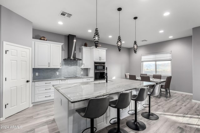 kitchen featuring white cabinetry, wall chimney exhaust hood, a spacious island, and decorative light fixtures