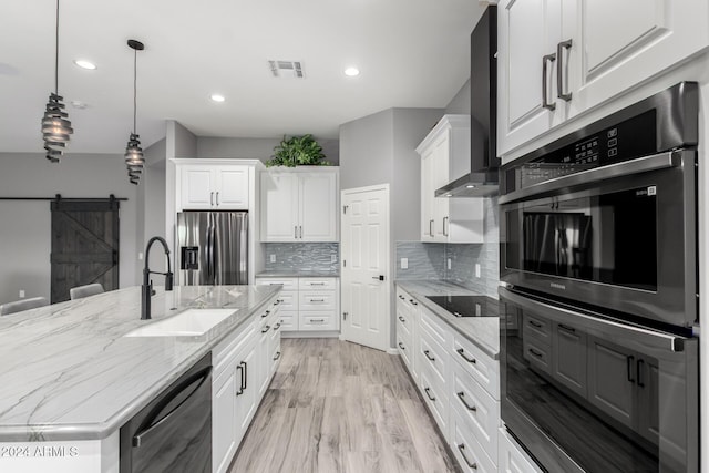 kitchen featuring white cabinets, wall chimney range hood, sink, a barn door, and appliances with stainless steel finishes