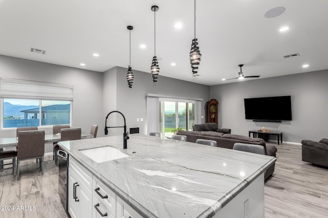 kitchen with sink, ceiling fan, decorative light fixtures, light stone counters, and white cabinetry