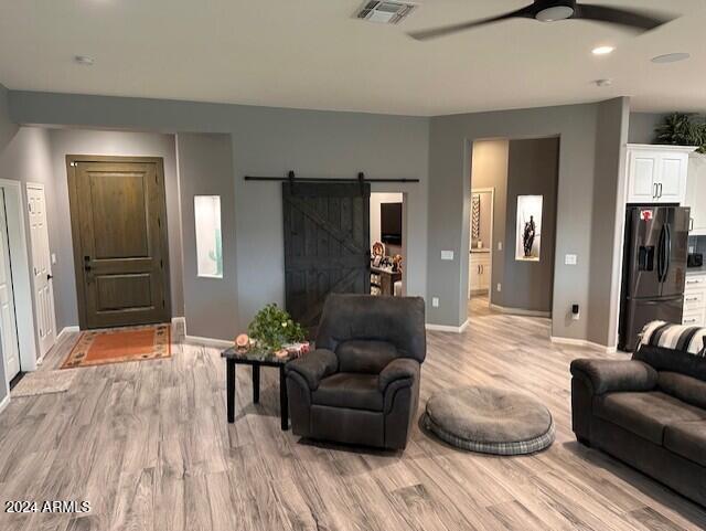 living room featuring a barn door, ceiling fan, and light hardwood / wood-style floors