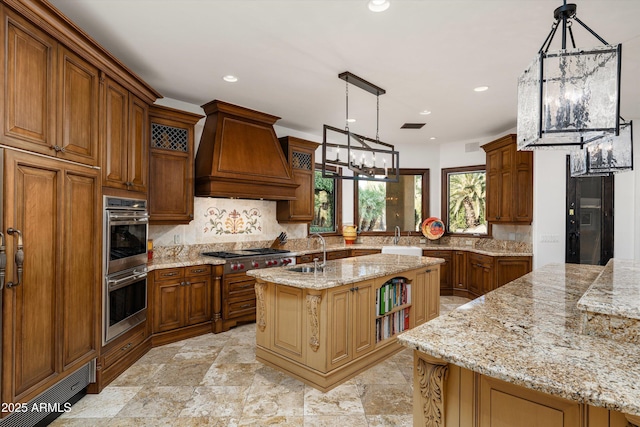 kitchen with custom exhaust hood, light stone countertops, pendant lighting, and a center island with sink