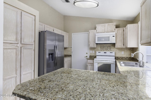 kitchen featuring light brown cabinetry, lofted ceiling, sink, decorative backsplash, and white appliances